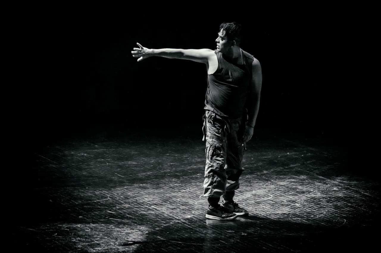 A male dancer in motion on a dimly lit stage captured in black and white.